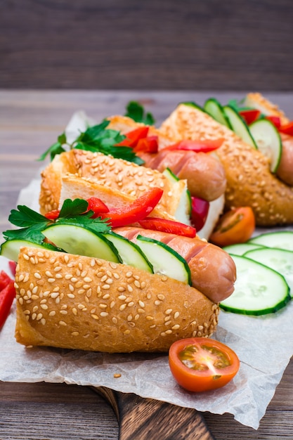 Hot dog pronti da salsicce fritte, panini al sesamo e verdure fresche su un tagliere su un tavolo di legno