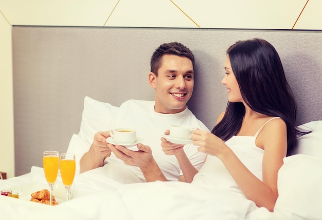 hotel, viaggi, relazioni e concetto di felicità - coppia sorridente che fa colazione a letto nella camera d'albergo