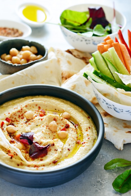 Hummus classico in una ciotola con erbe, pane pita, bastoncini di verdure e lattuga