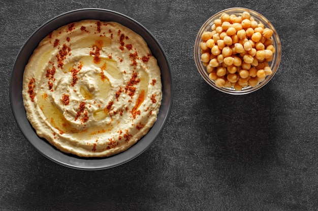 Hummus con olio e pepe rosso macinato e ceci su sfondo scuro vista dall'alto spazio per copiare il testo