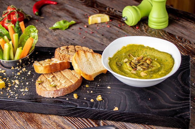 Hummus con spinaci, avocado e semi di zucca in una ciotola su una tavola di legno e bruschetta, cucina orientale