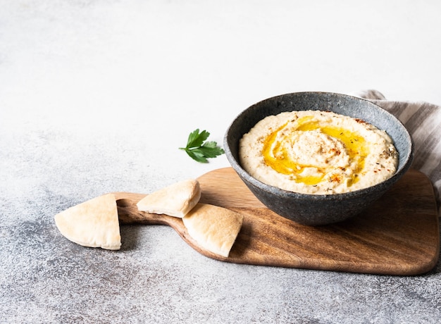 Hummus di ceci casalingo tradizionale in ciotola, condito con olio d'oliva e spezia secca della paprica sul tagliere di legno.