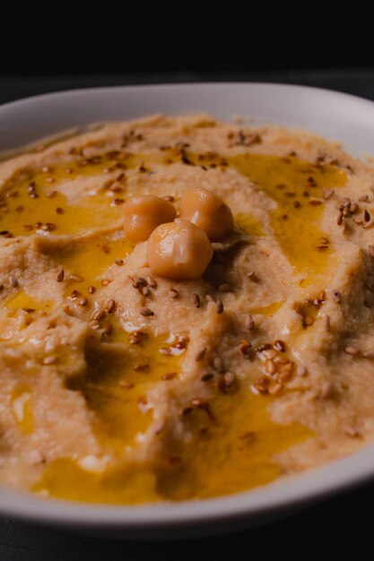 Hummus di ceci con olio d'oliva e sesamo tostato su fondo scuro e fuoco selettivo