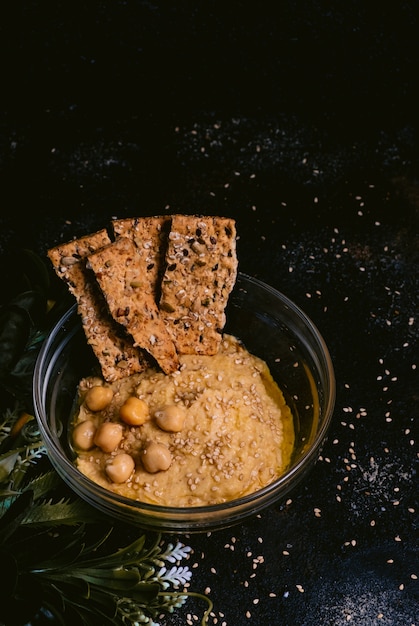 Hummus di ceci con sesamo in ciotola di vetro sulla tavola di legno. Cibo vegano