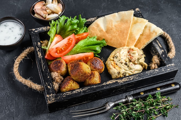 Hummus di ceci tradizionali fatti in casa, falafel, pane pita e verdure fresche. Sfondo nero. Vista dall'alto.