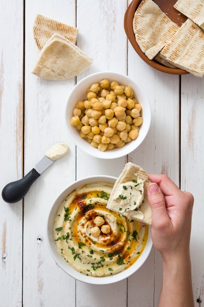 Hummus di immersione della donna in ciotola su una tavola di legno bianca rustica