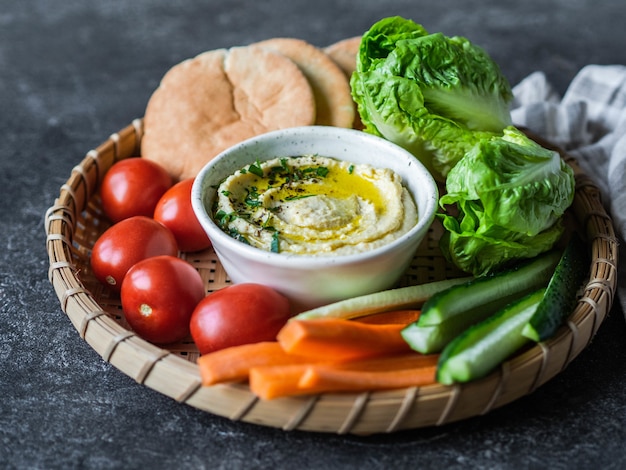 Hummus diffusione tradizionale fatta in casa tuffo servito con verdure fresche, pita ed erbe nel vassoio.