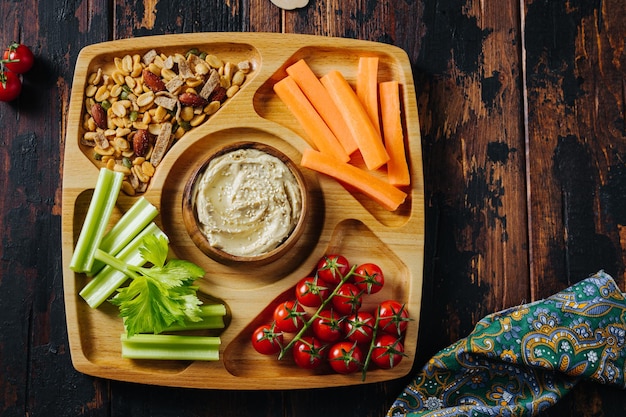 Hummus e bastoncini di verdure di carota e sedano su un piatto di legno