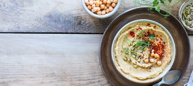 Hummus, salsa di ceci con olio d'oliva affumicato della paprica in una ciotola di ceramica su un fondo di legno. Vista dall'alto. Copia spazio.