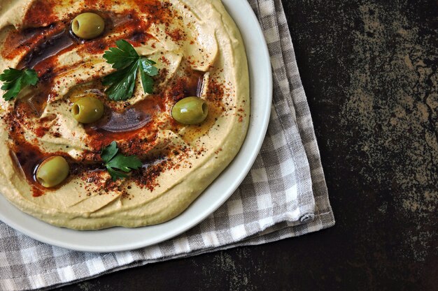 Hummus su un piatto con paprika, olio d'oliva e olive. Hummus classico fatto in casa fresco. Cucina mediorientale.