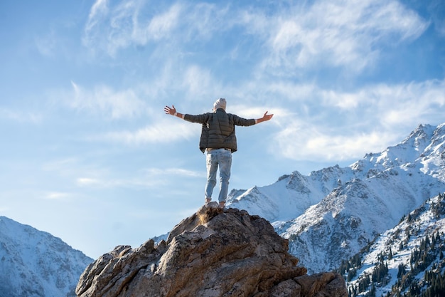 Hyped uomo in piedi su una roccia circondata da montagne innevate e cielo