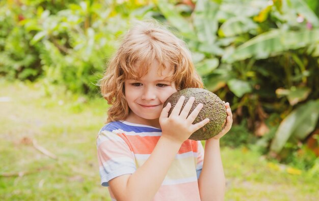 I bambini carini o ragazzini sorridono e tengono in mano il frutto dell'avocado