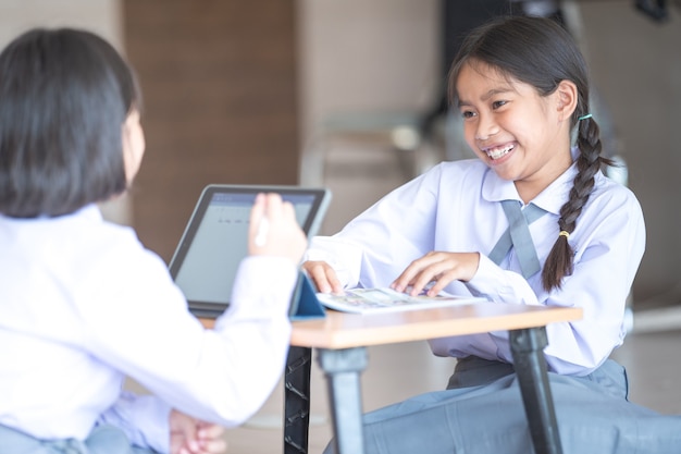 I bambini che tornano a scuola studiano insieme utilizzando la tavoletta digitale e scrivono sul taccuino a scuola