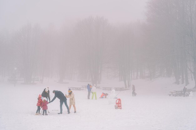 I bambini con gli adulti fanno degli uomini di neve in una pianura innevata e nebbiosa