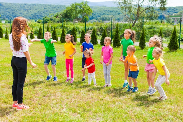 I bambini con l'insegnante si divertono all'aperto sul prato verde nel campo estivo