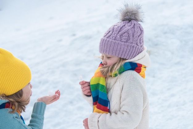 I bambini d'inverno soffiano la neve. Amici dei bambini felici che si divertono, giocano durante la passeggiata invernale all'aperto.