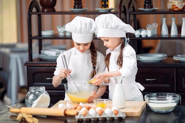 I bambini delle ragazze divertenti stanno preparando l'impasto in cucina.