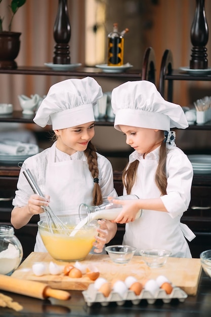 I bambini delle ragazze divertenti stanno preparando l'impasto in cucina.