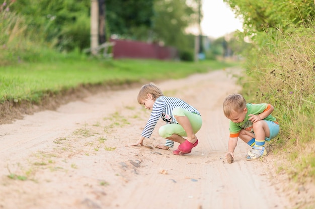 I bambini disegnano con una pietra sulla sabbia mentre si accovacciano sulla strada sabbiosa di un villaggio.