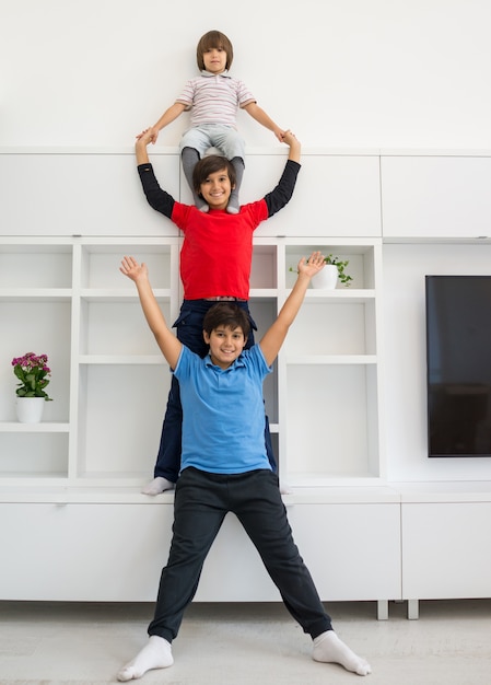 I bambini divertenti allegri che si divertono e che posano allineano sulle spalle nella nuova casa moderna