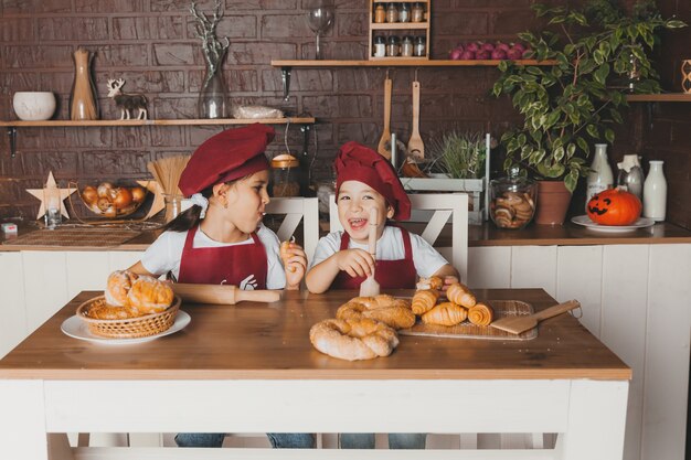 I bambini divertenti stanno preparando l'impasto, cuocendo i biscotti in cucina. Piccoli cuochi in grembiule tengono i dolci pasquali vicino agli occhi.