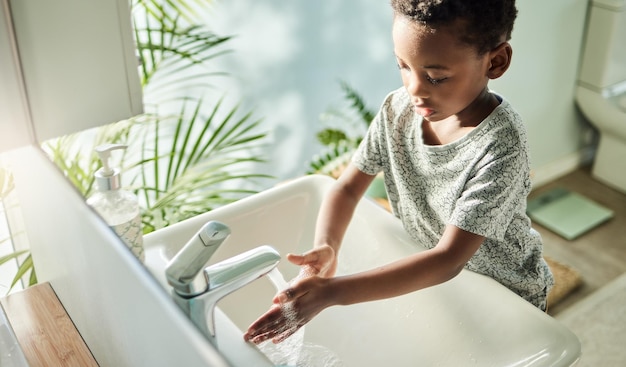 I bambini dovrebbero lavarsi spesso le mani con acqua e sapone Inquadratura dall'alto di un ragazzo che si lava le mani a un rubinetto in un bagno a casa