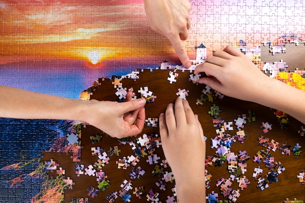 I bambini e le mani degli adulti impilano un puzzle di colore su una tavola di legno