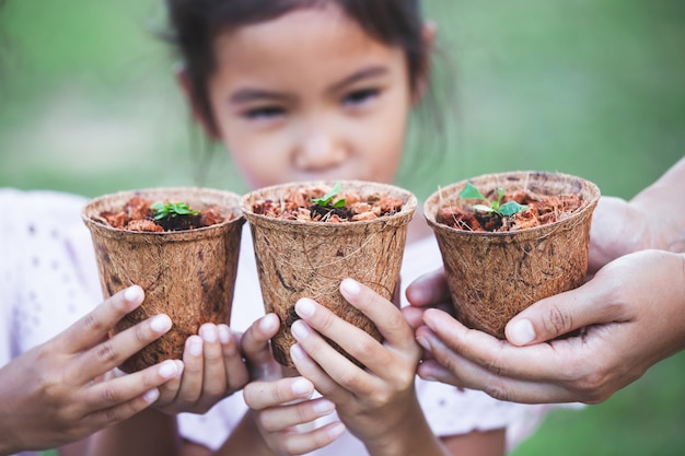 I bambini e le mani dei genitori che tengono le giovani piantine dentro riciclano insieme i vasi di fibra