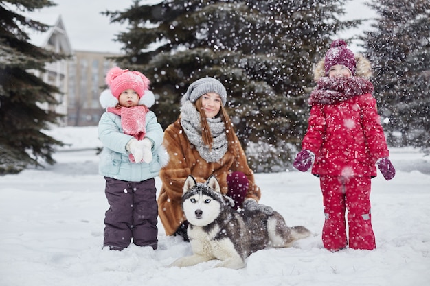 I bambini escono e giocano con il cane husky in inverno. I bambini si siedono sulla neve e accarezzarono il cane husky. Passeggiata nel parco in inverno, gioia e divertimento, cane husky con gli occhi blu. Russia, Sverdlovsk,
