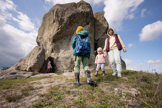 I bambini esplorano la natura I bambini indossano lo zaino per fare escursioni con la madre vicino a una grande pietra sulla collina Pidkamin Ucraina