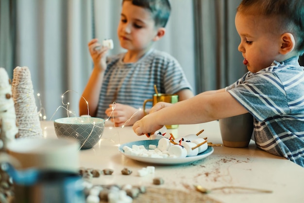 I bambini fanno pupazzi di neve con marshmallow e cannucce salate bevono cacao nella cucina di casa preparando ...