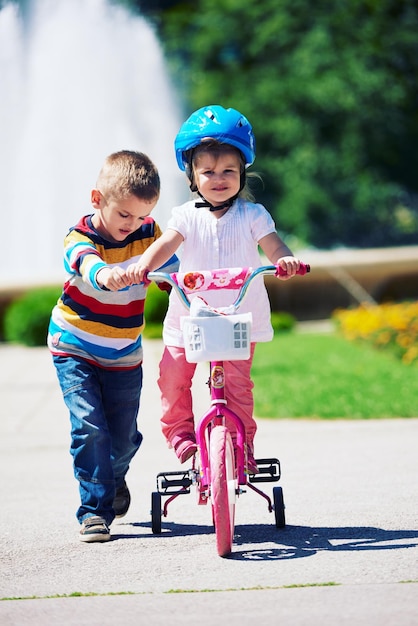 I bambini felici all'aperto, fratello e sorella nel parco si divertono. Ragazzo e ragazza nel parco che imparano ad andare in bicicletta.