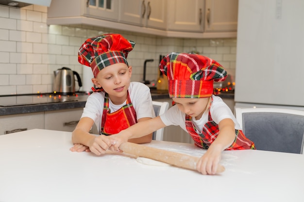 I bambini felici cucinano i biscotti di Natale a casa in cucina in costume da chef, ragazzo e ragazza