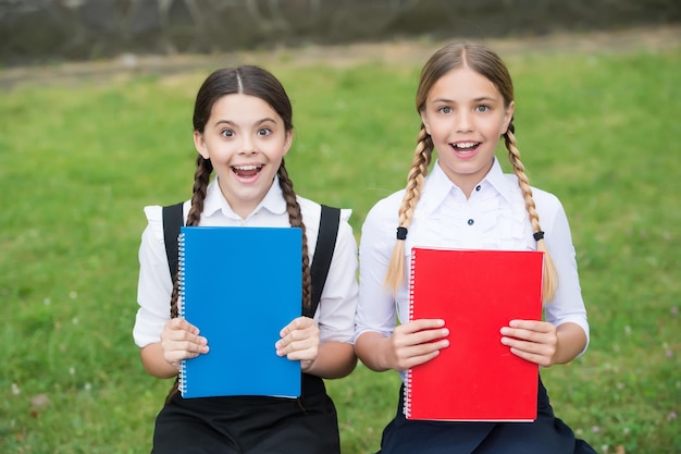 I bambini felici in uniforme scolastica mostrano libri scolastici colorati copertine di libri all'aperto