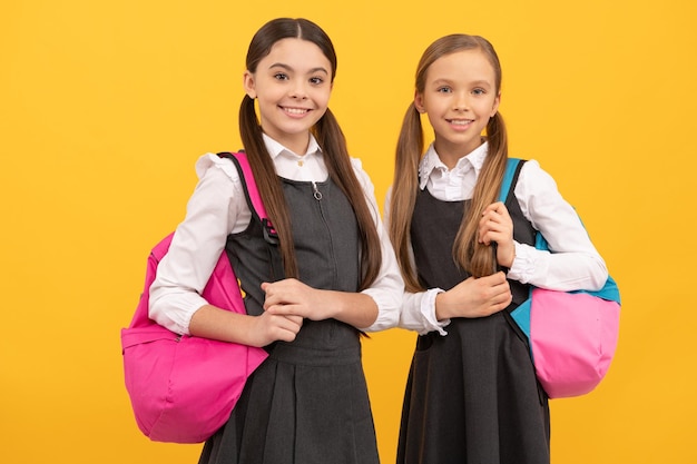 I bambini felici portano le borse della scuola in uniformi di moda formali su sfondo giallo per tornare a scuola