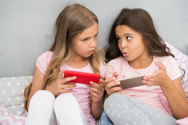 I bambini giocano all'applicazione di gioco mobile per smartphone. Concetto di applicazione per smartphone. Pigiama party da ragazzina per il tempo libero. Ragazze smartphone piccoli blogger. Esplora il social network. Smartphone per l'intrattenimento.