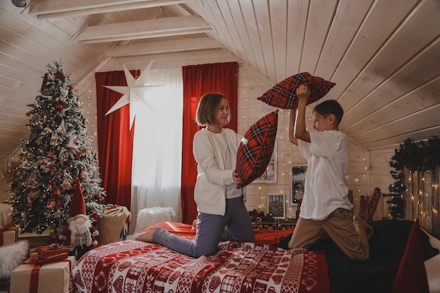 I bambini giocano con i cuscini sul letto nella camera da letto decorata per Natale, combattimenti di cuscini, il concetto delle vacanze di Capodanno