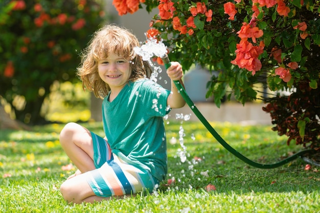 I bambini giocano con il tubo da giardino dell'acqua in cortile Divertimento estivo per bambini all'aperto Ragazzino che gioca con l'acqua h