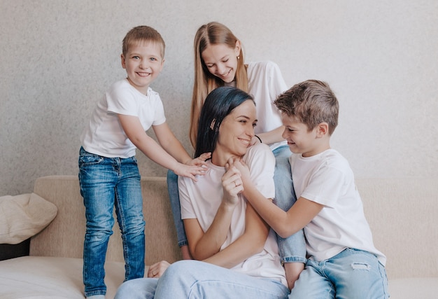 I bambini giocano e giocano con la madre seduta a casa sul divano. mamma felice, relazioni familiari perfette felici.