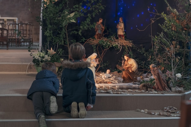 I bambini guardano il presepe di Natale con Giuseppe Maria e il piccolo Gesù in un presepe