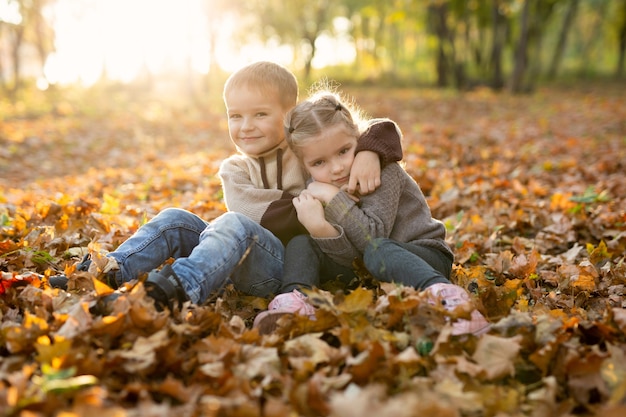 I bambini, il ragazzo e la ragazza svegli stanno giocando, sedendosi e abbracciando insieme nel parco di autunno.