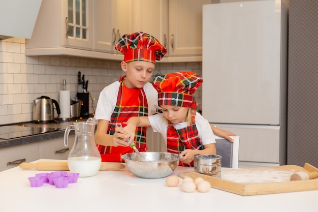 I bambini in costume da chef preparano l'impasto con farina, latte, uova e burro per i dolci di Natale