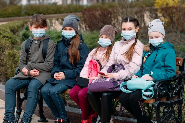 I bambini in età scolare in maschera medica siedono su una panchina.