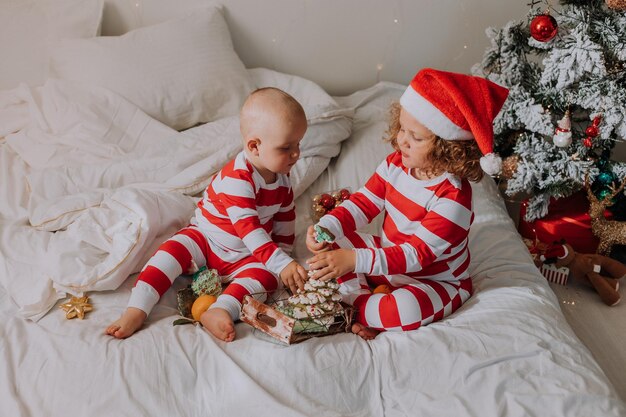 I bambini in pigiama bianco e rosso mangiano dolci natalizi seduti a letto. fratello e sorella, ragazzo e ragazza condividono i regali. mattina di natale. stile di vita. spazio per il testo. Foto di alta qualità