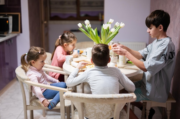 I bambini mangiano frutta e dessert bevono il tè a casa nella cucina serale Cioccolato su un bastoncino da sciogliere