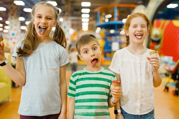 I bambini mangiano il gelato nel centro di intrattenimento. Svaghi di ragazzo e ragazze in vacanza, felicità infantile, bambini felici nel parco giochi