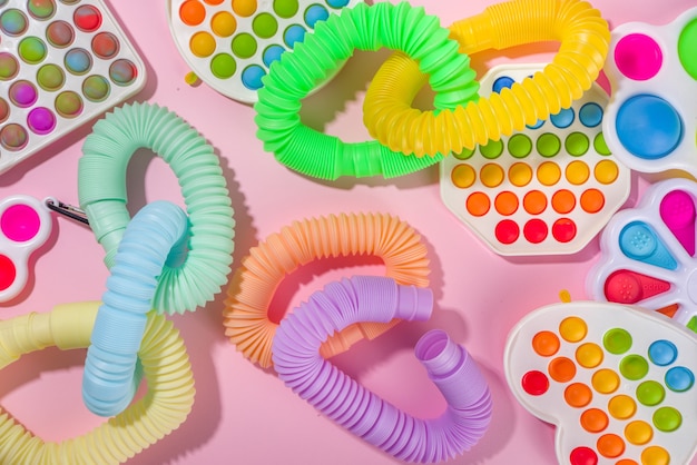 I bambini moderni alla moda agitano i giocattoli per le dita, il concetto di relax - set di diversi pop-it luminosi, semplici fossette, squishy, pop-tubi, su sfondo rosa colorato, spazio di copia vista dall'alto