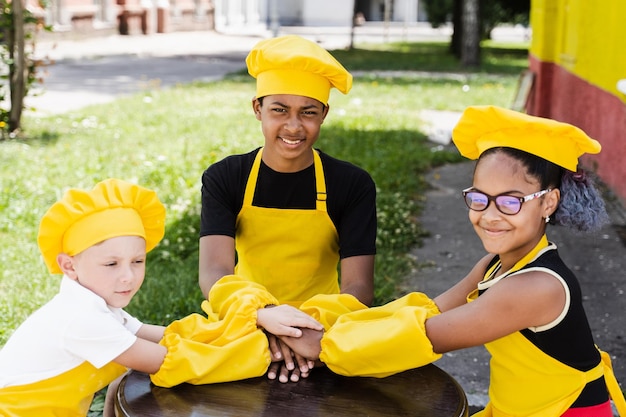 I bambini multirazziali cucinano toccando le mani insieme formando un mucchio Amicizia di bambini multinazionali I cuochi dell'infanzia con cappello da chef e uniforme grembiule giallo si mettono le mani l'uno sull'altro