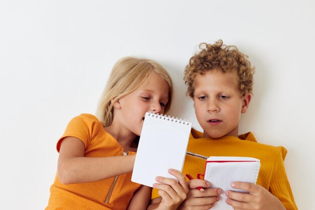 I bambini piccoli giacciono sul pavimento con blocchi per appunti e matite isolati sullo sfondo inalterato