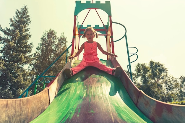 I bambini scivolano nel parco giochi all'aperto. I bambini giocano nel soleggiato parco estivo. Centro di attività e divertimento nella scuola materna o nel cortile della scuola. Bambino sulla diapositiva colorata.